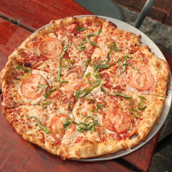 A Cowgirl Kitchen pizza with tomato slices and basil on a red wooden table.