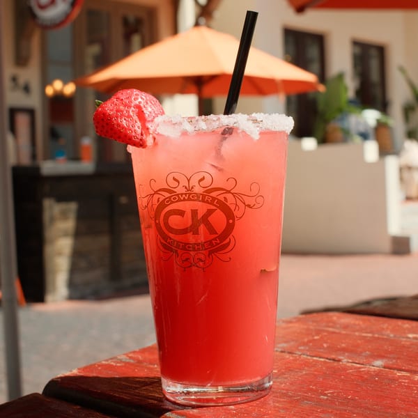 Cowgirl Kitchen's pink strawberry drink with a salted rim and black straw on a red wooden table.