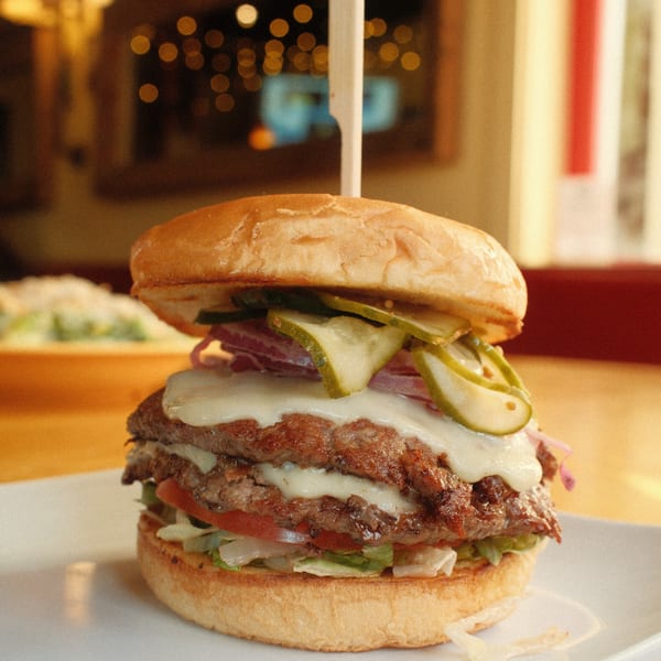 Double cheeseburger with pickles, onions, lettuce, and tomato on a bun, served at Cowgirl Kitchen.