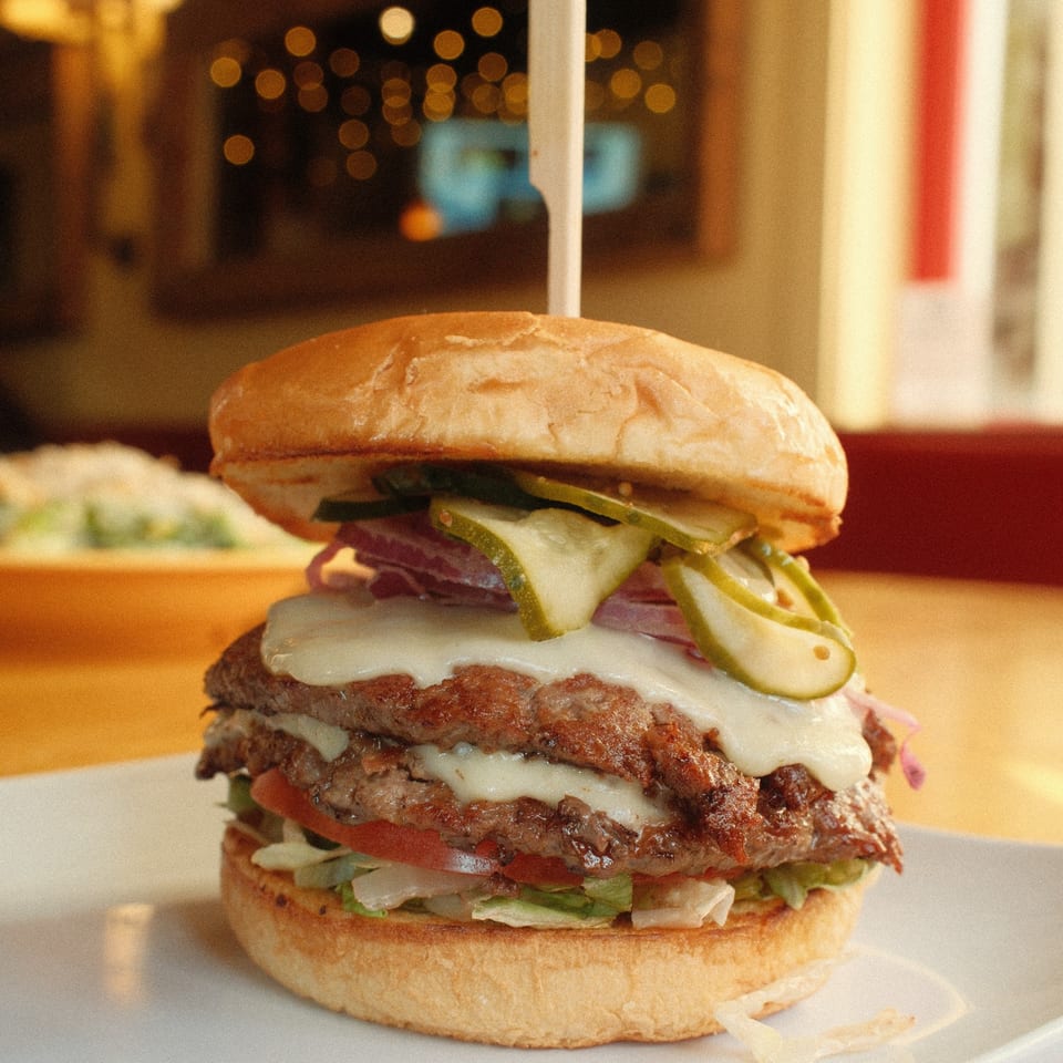 Double cheeseburger with pickles, onions, lettuce, and tomato on a bun, served at Cowgirl Kitchen.