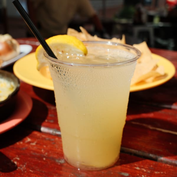 A cold drink with a lemon wedge and black straw, with tortilla chips in the background.