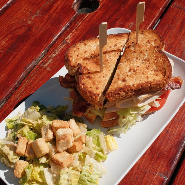 A toasted club sandwich with bacon, turkey, lettuce, and tomato, served with a side salad.
